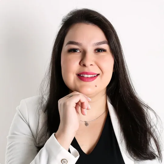 Dra. Veronica Favoni, mulher branca, cabelos castanhos escuros abaixo dos ombros, camisa preta e blazer branco.